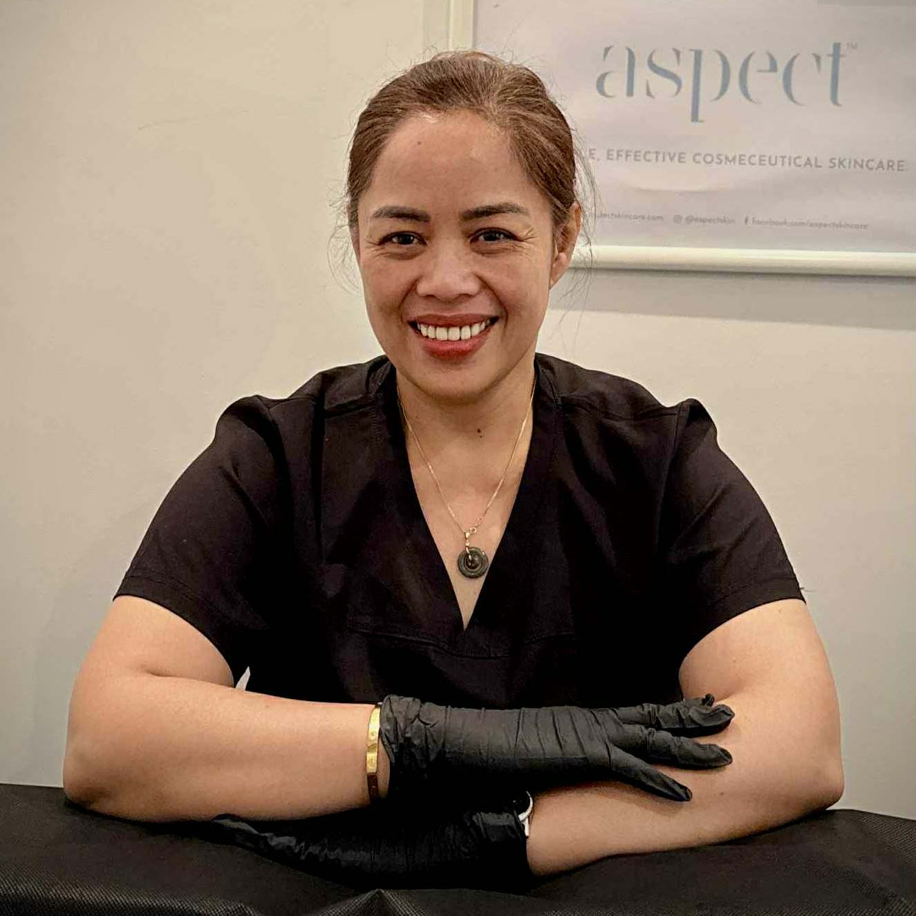 Woman in a black shirt and gloves sitting at a desk with skincare products in the background